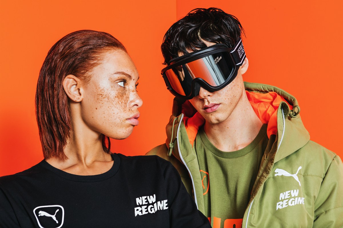Portrait de deux modèles portant la collection Atelier New Regime × PUMA sur fond orange